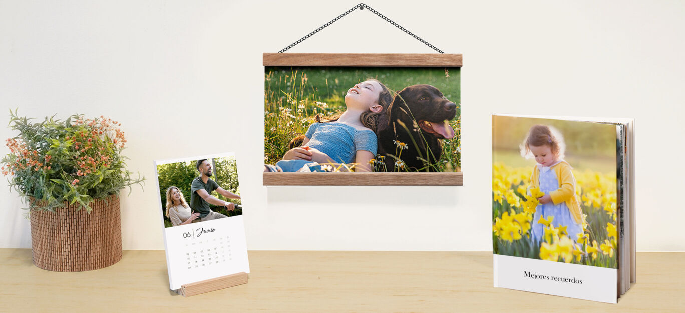 Productos personalizados CEWE: lámina con marco de madera, calendario de sobremesa y álbum de fotos, sobre una mesa de madera.